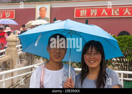 Coppia turistica cinese che si protegge dalla pioggia con ombrelloni in una giornata umida in Piazza Tienanmen, Pechino, Cina. Ritratto del Presidente Mao TSE Tung orologi dalle mura della città Proibita. (125) Foto Stock