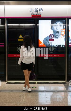 Giovane donna cinese in viaggio attende un treno della metropolitana della linea 5 per arrivare al binario Beixinqiao, una moderna stazione sicura di interscambio con porta di sicurezza. (125) Foto Stock