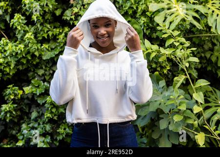 Ritratto di una donna afroamericana felice che indossa una felpa bianca con cappuccio in giardino Foto Stock