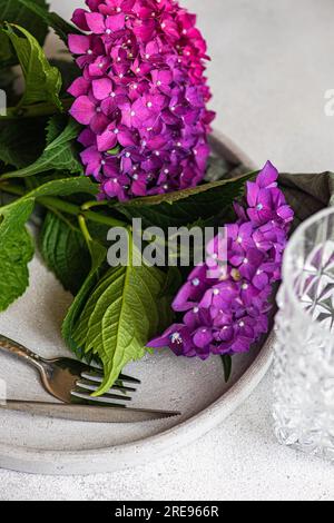 Vista dall'alto dell'ortensia viola posizionata su un tavolo bianco vicino a lastre di ceramica e vetro Foto Stock