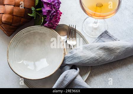 Vista dall'alto dell'ortensia viola posta su un tavolo bianco vicino a piatti di ceramica e bicchiere con bevanda Foto Stock