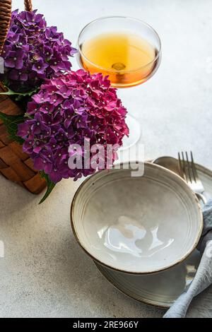 Vista dall'alto dell'ortensia viola posta su un tavolo bianco vicino a piatti di ceramica e bicchiere con bevanda Foto Stock