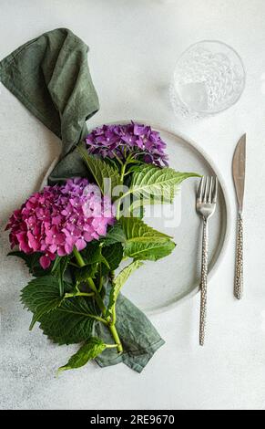 Vista dall'alto dell'ortensia viola posizionata su un tavolo bianco vicino a lastre di ceramica e vetro Foto Stock
