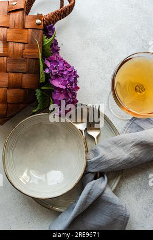 Vista dall'alto dell'ortensia viola posta su un tavolo bianco vicino a piatti di ceramica e bicchiere con bevanda Foto Stock