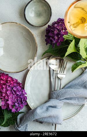 Vista dall'alto dell'ortensia viola posta su un tavolo bianco vicino a piatti di ceramica e bicchiere con bevanda Foto Stock