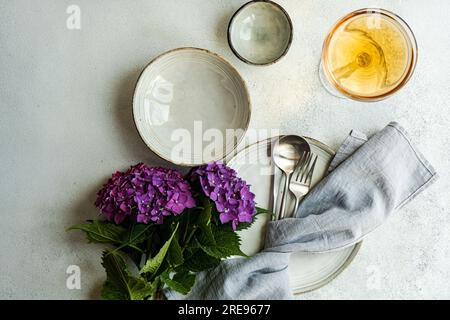 Vista dall'alto dell'ortensia viola posta su un tavolo bianco vicino a piatti di ceramica e bicchiere con bevanda Foto Stock