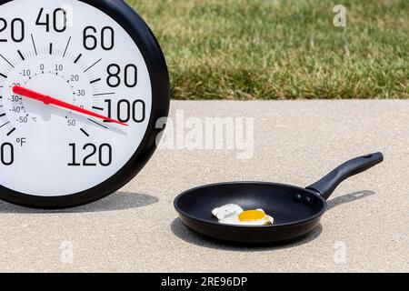 Cuocere l'uovo sul marciapiede con il termometro al sole durante l'onda di calore. Concetto di allarme per temperature elevate, temperature elevate e calore. Foto Stock