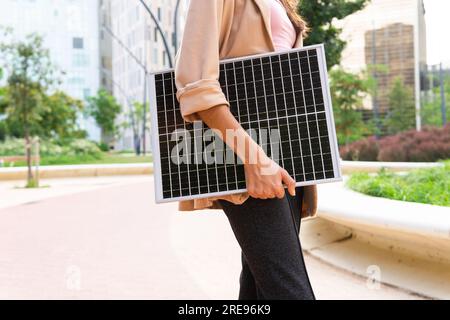 Dal basso, irriconoscibile imprenditrice donna in un blazer in piedi per strada con pannello solare portatile Foto Stock