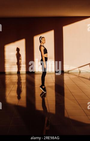Giovane atletica caucasica che lavora al tramonto, ombre e luce sullo sfondo Foto Stock
