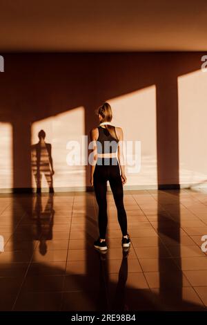 Vista posteriore di una giovane donna caucasica atletica anonima al tramonto, ombre e luce sullo sfondo Foto Stock