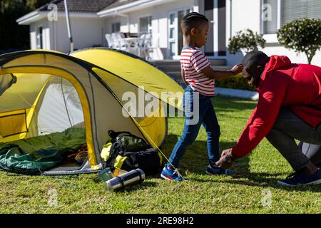 Felice padre e figlio afroamericano che mette la tenda in un giardino soleggiato, spazio fotocopie Foto Stock