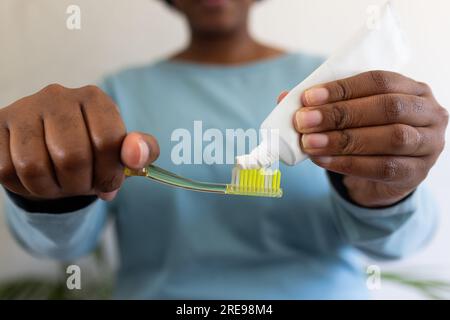 Mani di una donna afroamericana di taglia più grande che mette dentifricio sullo spazzolino da denti Foto Stock