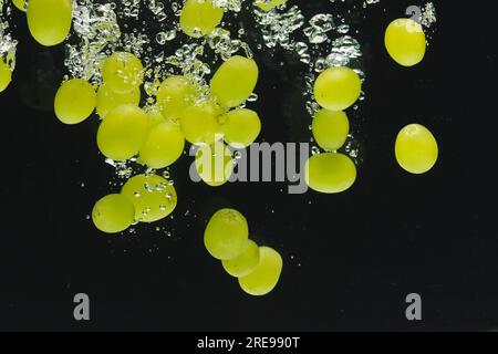 Primo piano di uva bianca che cade in acqua con spazio di copia su sfondo nero Foto Stock