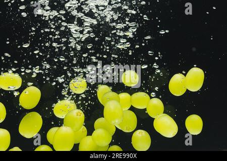 Primo piano di uva bianca che cade in acqua con spazio di copia su sfondo nero Foto Stock