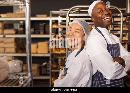 Ritratto di diversi panettieri felici che indossano grembiuli nel panificio con le braccia incrociate Foto Stock