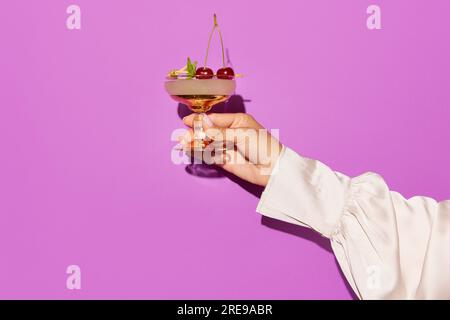 Donna che tiene a mano un cocktail aperol, ciliegie decorate su sfondo viola. Foto Stock