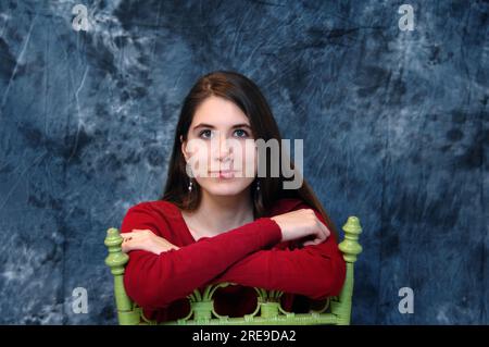 Una ragazza adolescente siede in una sedia di legno verde lime, girata all'indietro. Le sue braccia poggiano sul retro della sedia. Foto Stock