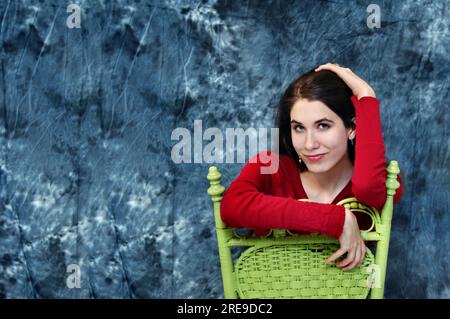 Appoggiata su una sedia girata all'indietro, questa adolescente sorride con gli occhi mentre si appoggia sul retro di una sedia di legno verde. Foto Stock