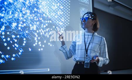 Giovane insegnante femminile che tiene una lezione di scienza dei dati a diversi gruppi multietnici di studenti femminili e maschili nella Dark College Room. Proiezione di una presentazione Foto Stock