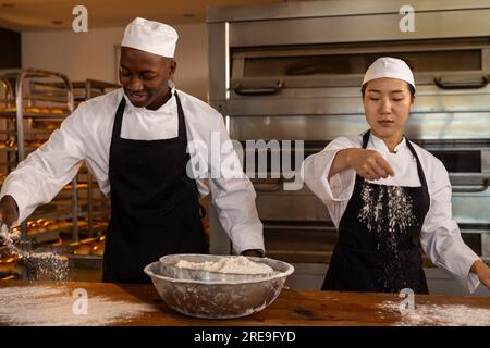 Forni diversi e felici che lavorano nella cucina dei prodotti da forno, versano farina e indossano grembiuli neri Foto Stock