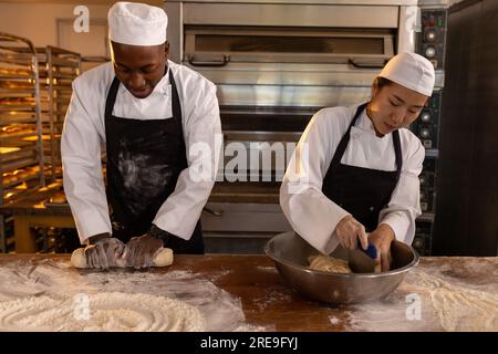 Diversi panettieri concentrati che indossano grembiuli nella cucina dei prodotti da forno, impastano e tagliano l'impasto Foto Stock