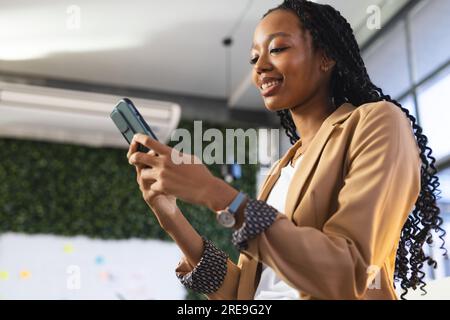 Donna d'affari afro-americana felice che usa lo smartphone in ufficio Foto Stock