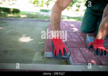 Un lavoratore poggia pietre di pavimentazione rosse su una superficie preparata in modo uniforme. Foto Stock