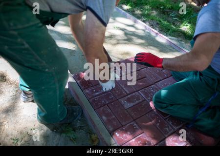 Un lavoratore inserisce le pietre di pavimentazione e l'altro le poggia in modo uniforme e preciso. Foto Stock