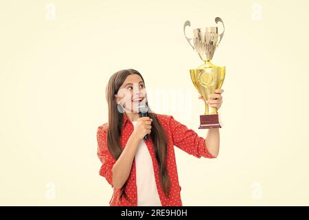 Ragazza adolescente in possesso di un trofeo microfono discorso. Il bambino vincitore ha vinto il concorso, celebrando il successo e la vittoria, il premio di successo. Foto Stock