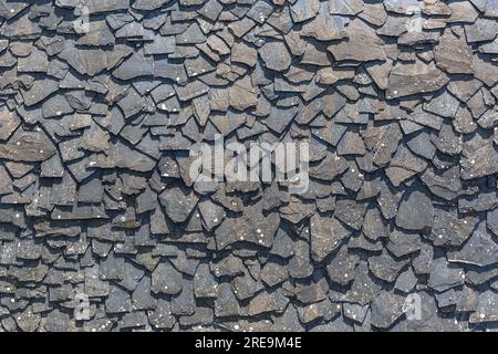 Vista dettagliata della struttura della parete rivestita in modo casuale con pannelli in ardesia, materiale tipico e tradizionale in pietra di scisto, utilizzato come rivestimento impermeabile esterno Foto Stock