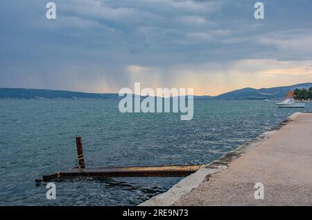 Cielo tempestoso sulla costa adriatica della Croazia a Kastel Kambelovac a Kastela, con un vecchio pontile arrugginito in primo piano. Tarda primavera Foto Stock