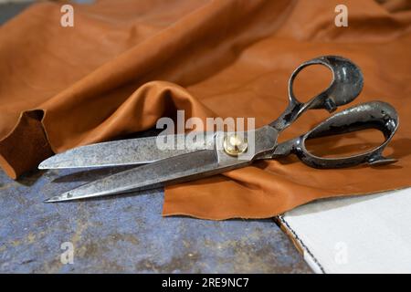 Grandi forbici vecchie che giacciono su un pezzo di pelle in un laboratorio di artigianato, spazio per la copia, messa a fuoco selezionata, profondità di campo ridotta Foto Stock