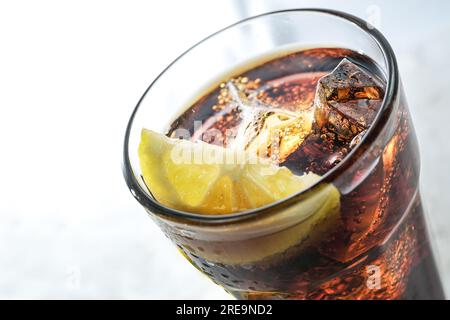 Parte di un bicchiere da bere con cola fresca, cubetti di ghiaccio e fetta di limone, rinfrescante bevanda dolce a base di caffeina su sfondo grigio chiaro, spazio copia, sele Foto Stock