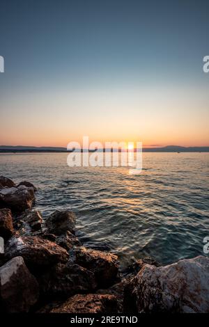 Spiaggia nascosta a Vrbnik sull'isola di Krk in Croazia. Bellissima spiaggia di pietra tra le rocce e all'alba Foto Stock