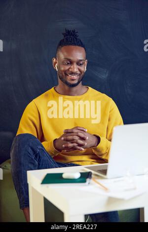 Giovane africano che lavora in remoto online, conduce videochiamate online con i colleghi, discutendo di progetti. Sorridendo Foto Stock