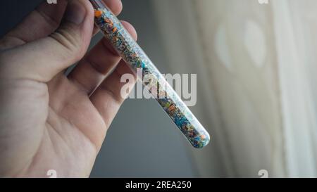 Foto macro di una provetta piena di microplastiche raccolte dalla spiaggia. Concetto di inquinamento idrico e gestione dei rifiuti industriali. Foto Stock