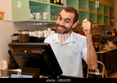 Il personale del ristorante è felice. Ritratto di un giovane uomo con barba corta che dà il pollice in alto Foto Stock