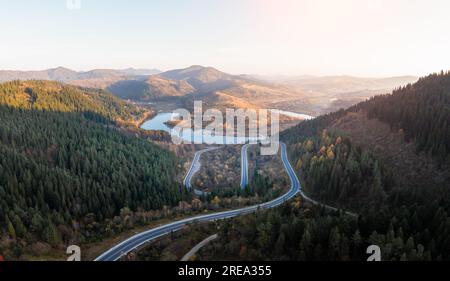 Panorama autunnale sulle montagne con strada di montagna a serpentina, fiume e foresta mista. Vista aerea con droni. Fotografia di paesaggi Foto Stock