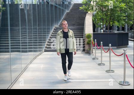 Joyful caucasian Guy passa davanti a un edificio commerciale. Foto Stock