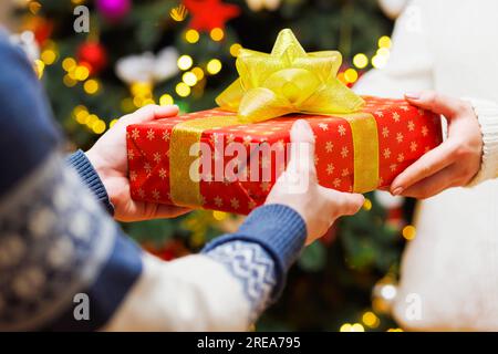 Mani maschili regalano un regalo in carta da regalo natalizia alle mani femminili Foto Stock