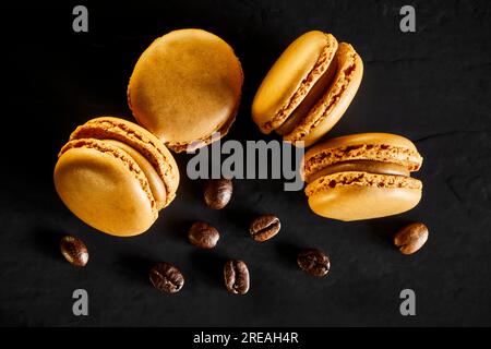 Macaron aromatizzati al caffè su sfondo scuro con chicchi di caffè. Foto Stock