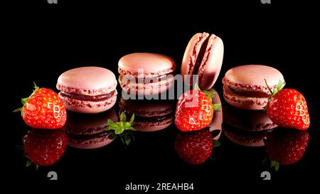 Macaron francesi con fragole su una superficie nera riflettente. Foto Stock