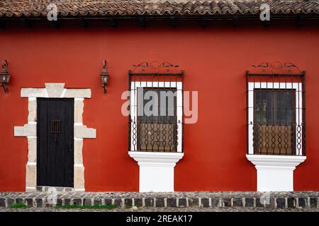 Porta d'ingresso e finestre con barre di sicurezza in una piccola casa vecchia dipinta di rosso in Guatemala Foto Stock