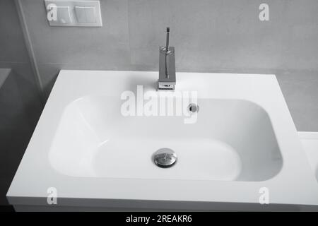 Moderno interno del bagno, lavabo bianco con cassetti, rubinetto cromato, presa e interruttore a parete. Interno del bagno con lavandino e rubinetto. Foto Stock