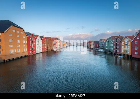 Colorati magazzini storici in legno con il fiume Nidelva nel quartiere Brygge di Trondheim, Norvegia, in inverno contro il cielo blu Foto Stock
