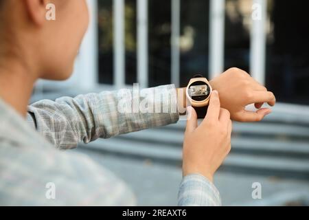 Donna che controlla il sistema di sicurezza domestica all'aperto tramite l'app smartwatch, primo piano. Immagine della stanza attraverso la telecamera CCTV sul display Foto Stock