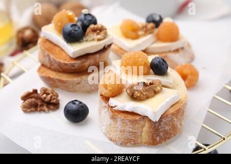 Gustosi panini con formaggio brie, frutti di bosco freschi e noci sul tavolo, primo piano Foto Stock