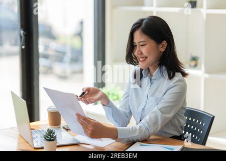 una giovane donna d'affari siede a un tavolo e legge un documento in ufficio Foto Stock