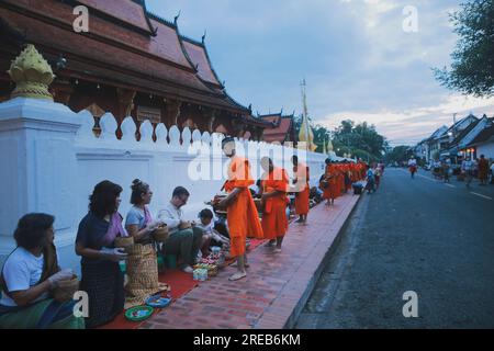 luang prabang laos - july20.2023 : villaggio e turista che offre riso appiccicoso al monaco buddista la mattina presto al più famoso landmar di wat sensoukharam Foto Stock