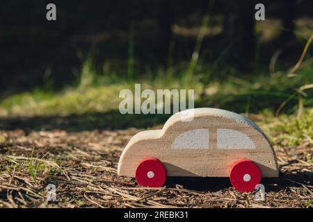 Macchinina giocattolo in legno su sfondo verde della foresta. Eco-car Concept World auto giorno libero veicolo elettrico ambiente trasporto auto elettrico. Ibrido elettrico. Motore sostenibile. Zero emissioni di CO2 per la consapevolezza naturale e il concetto di inquinamento ambientale verde Foto Stock